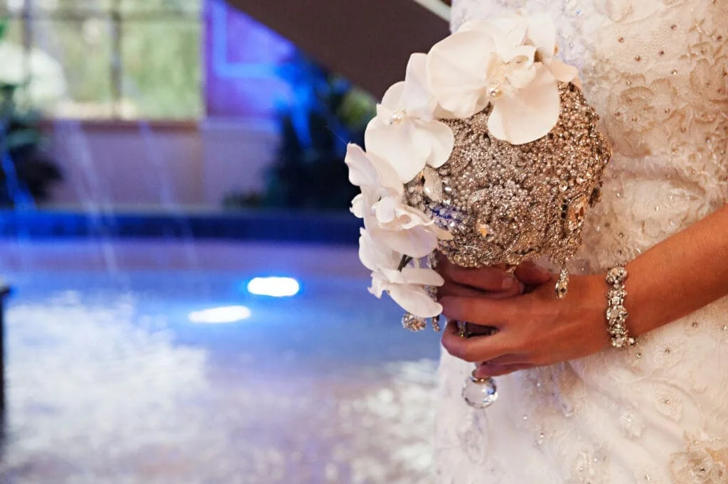 A bride holding a wedding bouquet in front of a fountain.